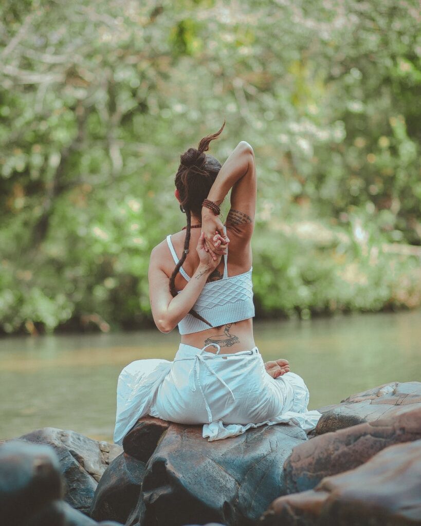 back view photo of a woman sitting near body of water doing yoga